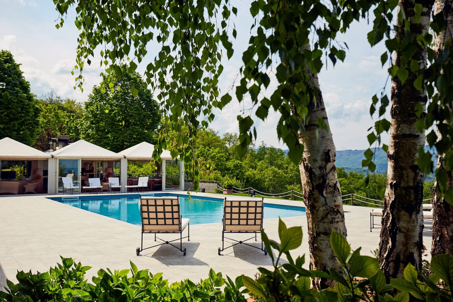 Luxury outdoor pool area with lounge chairs surrounded by lush greenery and shaded cabanas, offering a serene retreat. | Only on SopranoVillas
