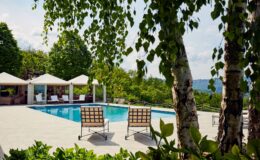 Luxury outdoor pool area with lounge chairs surrounded by lush greenery and shaded cabanas, offering a serene retreat.