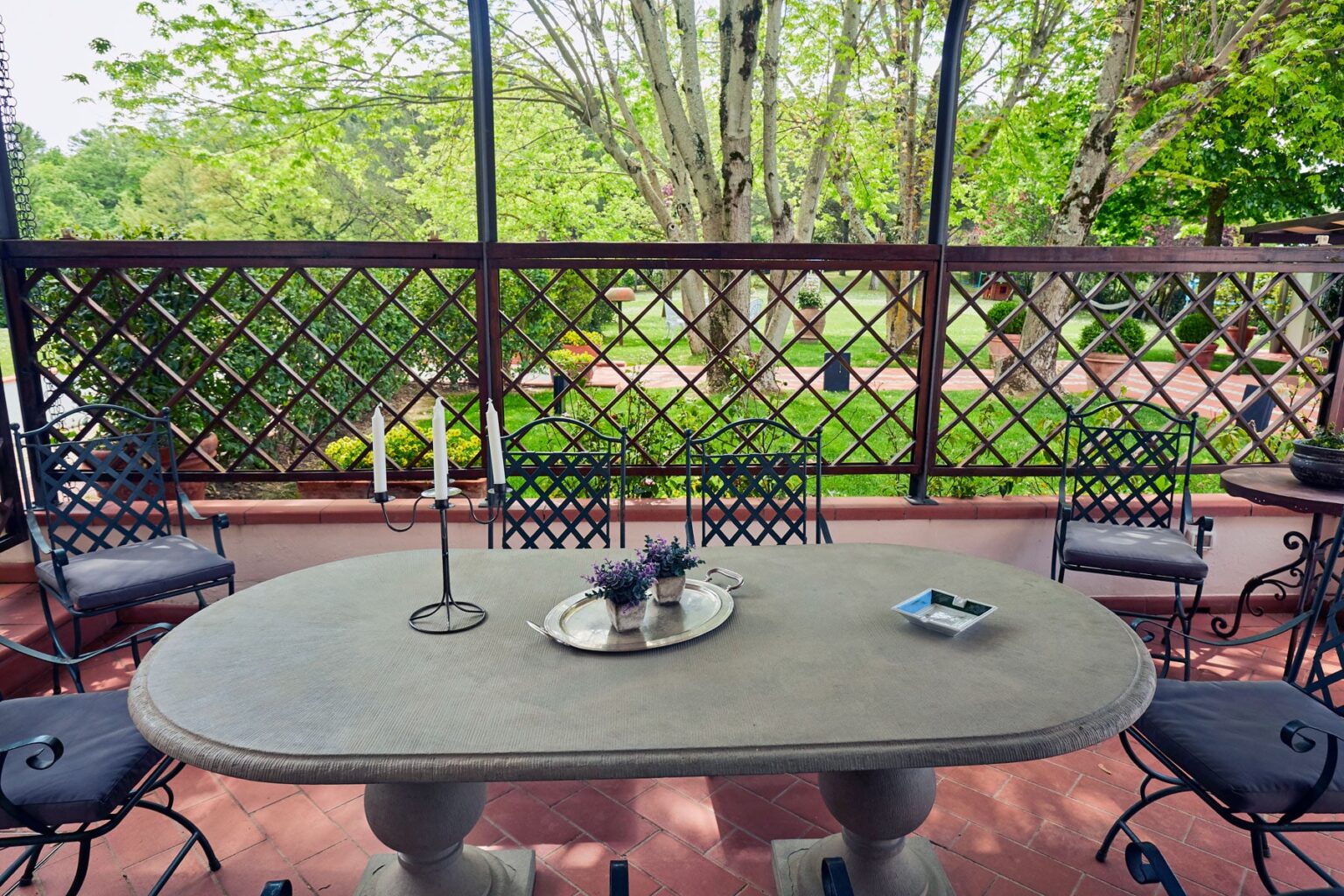 Outdoor patio featuring a stone table surrounded by decorative chairs, with a view of a lush garden through a lattice fence. Ideal for dining or relaxation in a serene environment. | Only on SopranoVillas