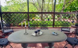 Outdoor patio featuring a stone table surrounded by decorative chairs, with a view of a lush garden through a lattice fence. Ideal for dining or relaxation in a serene environment.