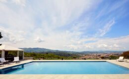 Luxury villa with a stunning infinity pool overlooking a scenic landscape, featuring mountains and a clear blue sky. Ideal for relaxation and outdoor gatherings.