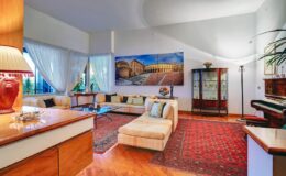 Spacious modern living room featuring a large sectional sofa, elegant wooden furniture, a decorative area rug, and a grand piano, complemented by natural light from large windows and a vibrant wall art piece.