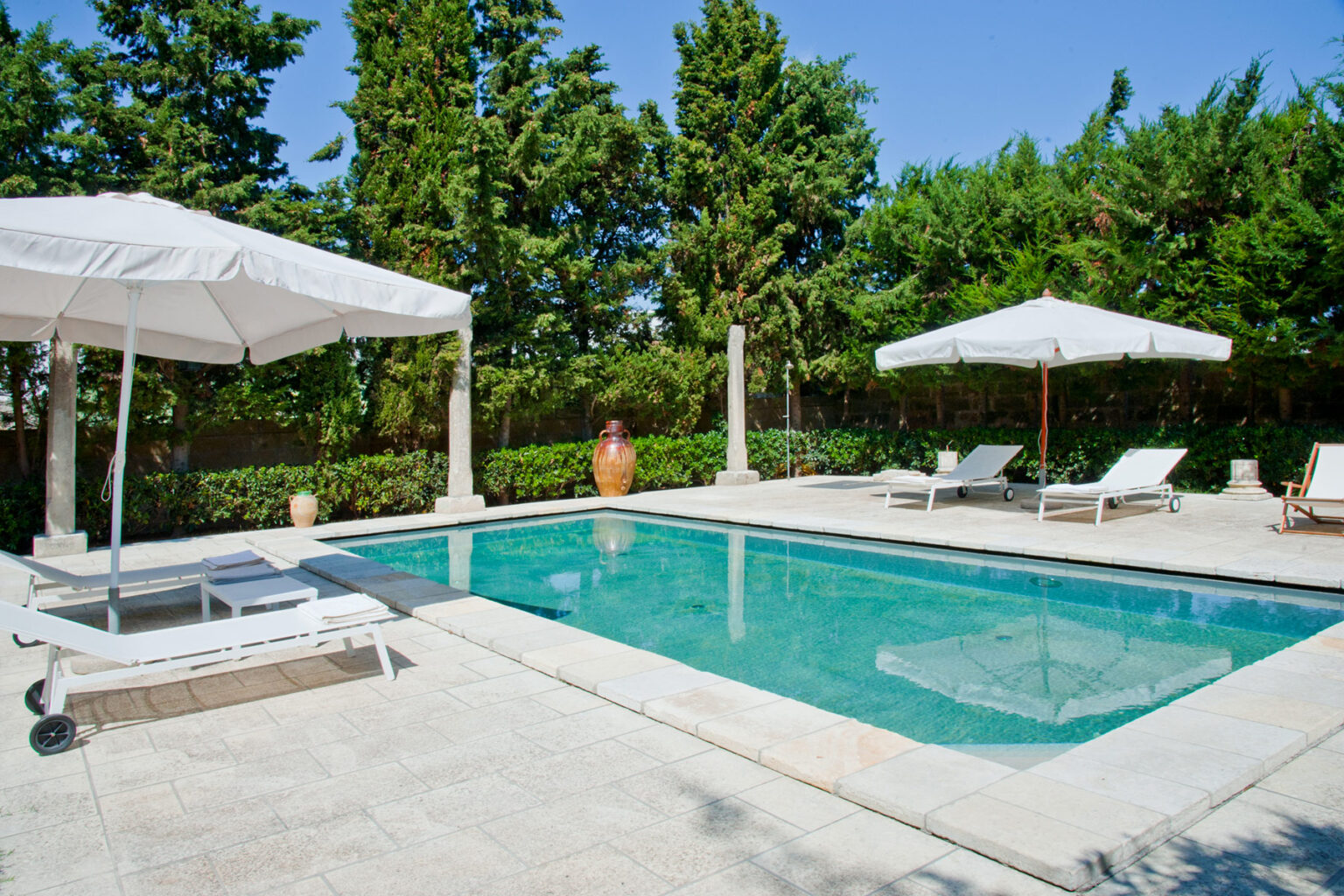 Luxury outdoor swimming pool surrounded by lush greenery, featuring sun loungers and umbrellas for relaxation. Ideal for summer leisure and outdoor gatherings. | Only on SopranoVillas