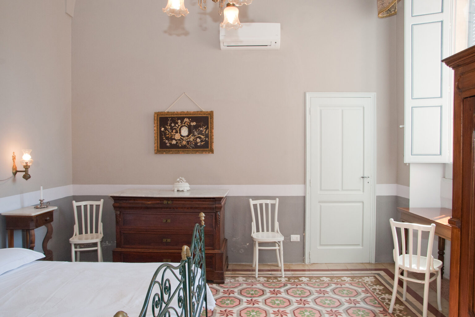 Cozy bedroom interior featuring a vintage bed, wooden furniture, and decorative wall art. The room has a warm color palette, air conditioning unit, and classic patterned tile flooring, creating a comfortable and inviting atmosphere. | Only on SopranoVillas