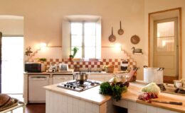 Bright and inviting kitchen with a modern design, featuring a gas stove, fresh vegetables on the countertop, and a window allowing natural light to illuminate the space. The walls are adorned with decorative tiles, creating a warm and welcoming atmosphere.