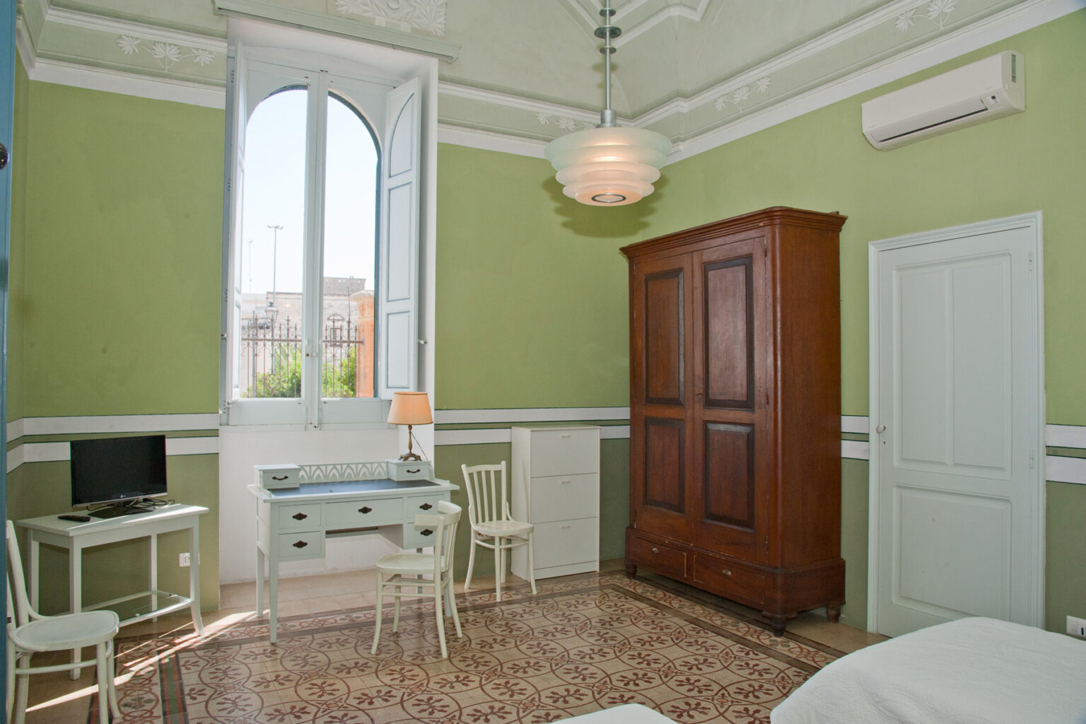 Bright and airy bedroom featuring green walls, large windows, a vintage wardrobe, a small desk with a chair, and a TV, creating a cozy and inviting atmosphere. | Only on SopranoVillas