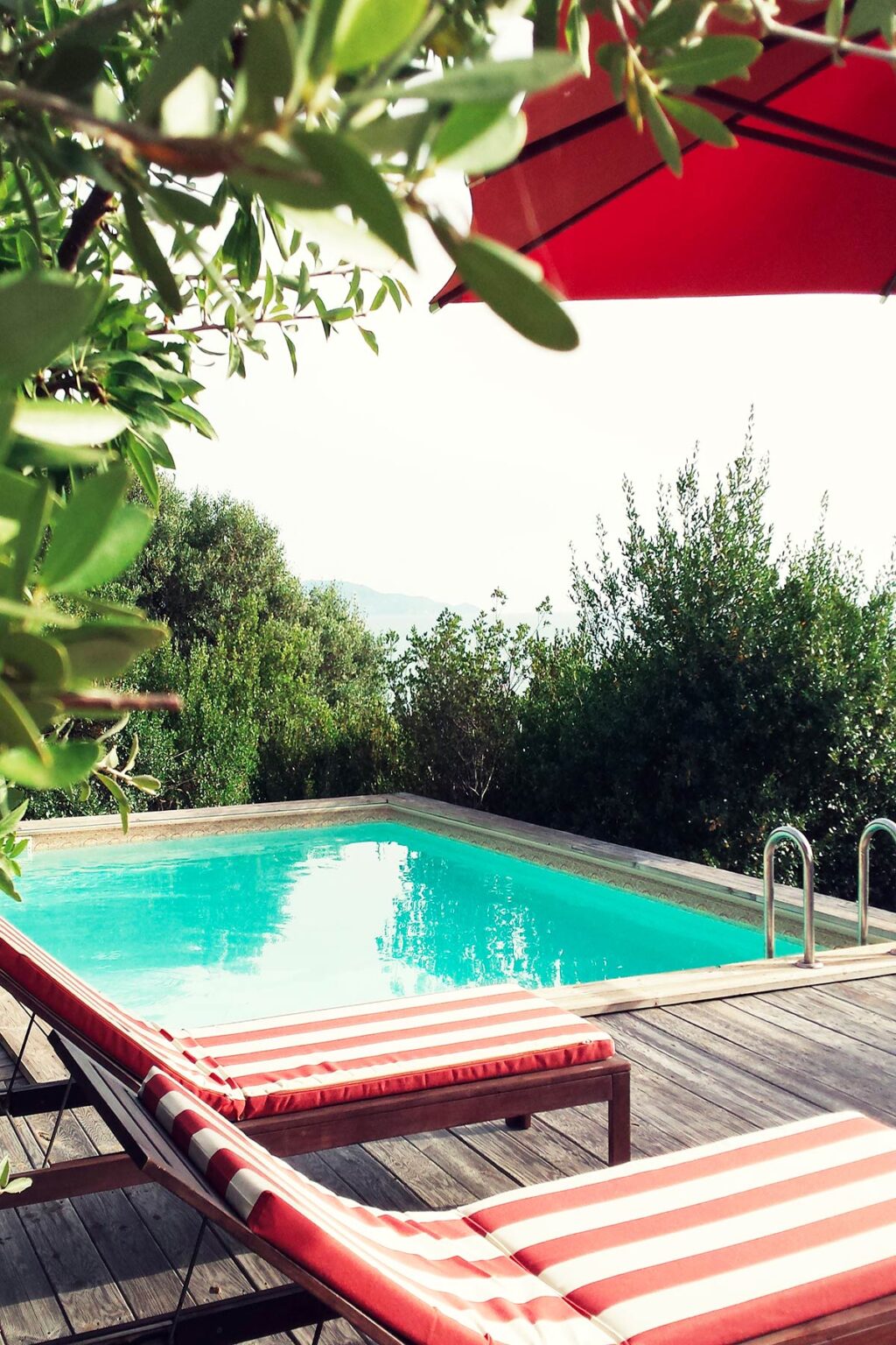 Serene outdoor swimming pool surrounded by lush greenery and trees, offering a tranquil escape with a scenic view in the background. | Only on SopranoVillas