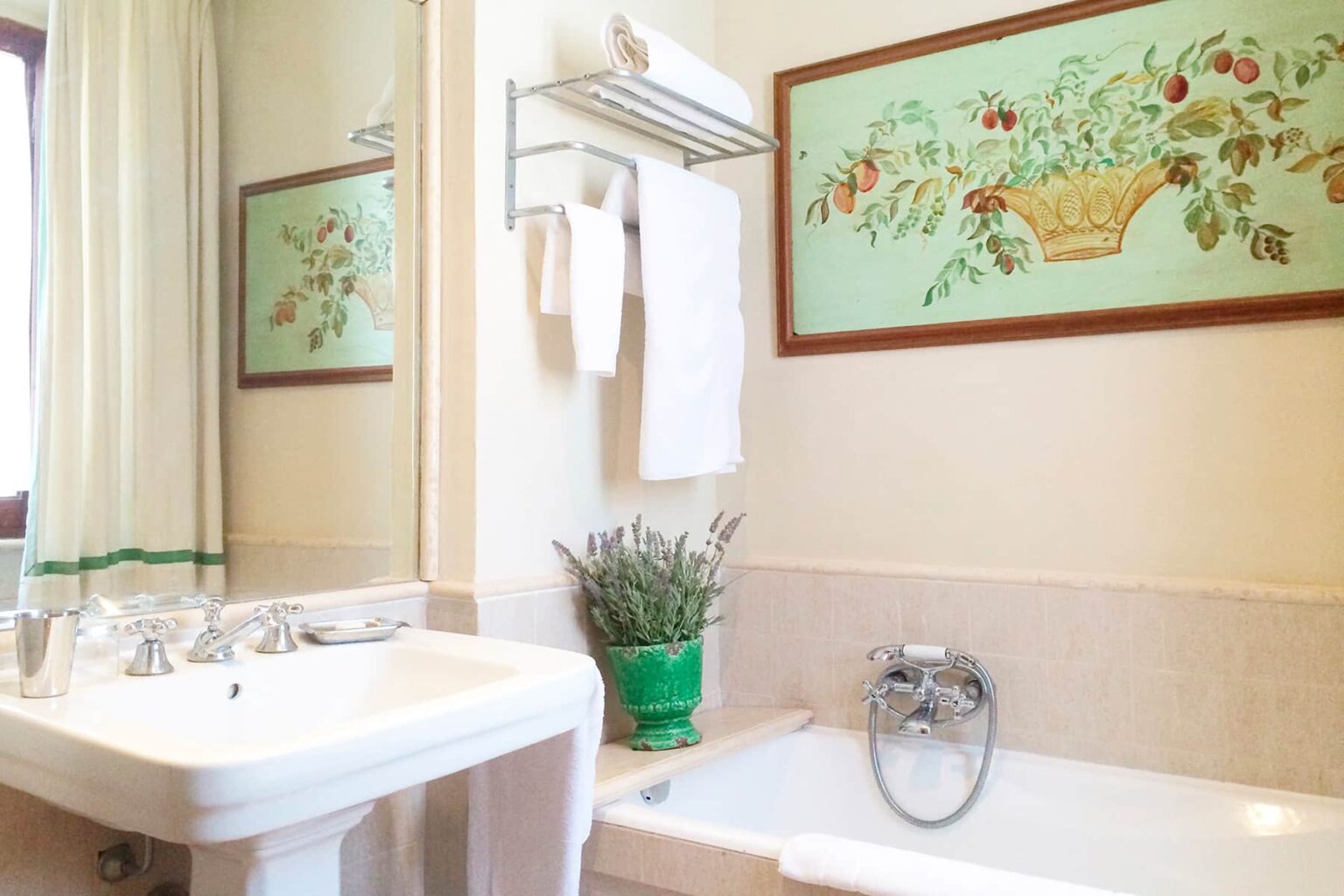 Bright and inviting bathroom featuring a white sink and a cozy bathtub, adorned with a green plant and decorative wall art depicting a floral basket. Soft curtains enhance the serene atmosphere, making it a perfect space for relaxation. | Only on SopranoVillas