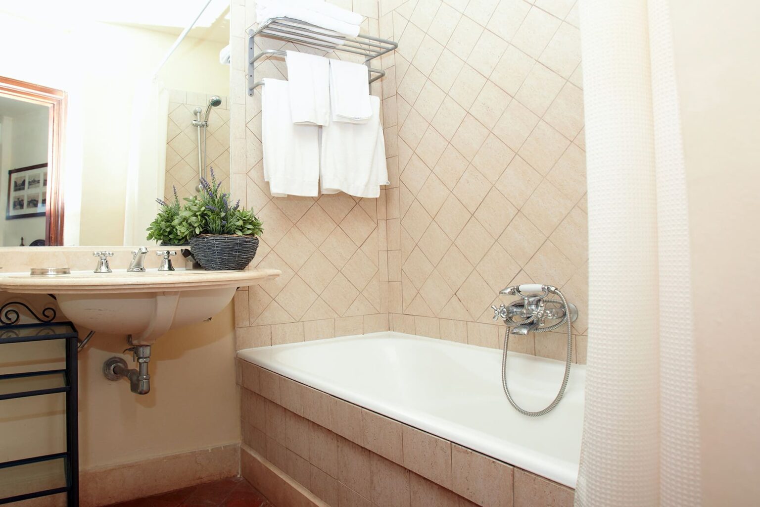 Modern bathroom featuring a white bathtub, a wall-mounted sink, and neatly arranged towels. The decor includes a small potted plant, enhancing the serene atmosphere. Ideal for showcasing stylish home interiors or bathroom renovation ideas. | Only on SopranoVillas