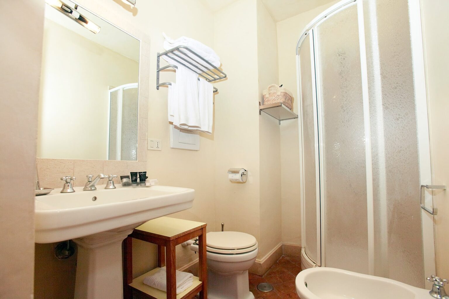 Modern bathroom featuring a double sink vanity, a shower stall, a toilet, and a small wooden stool, with towels neatly arranged on a rack. | Only on SopranoVillas