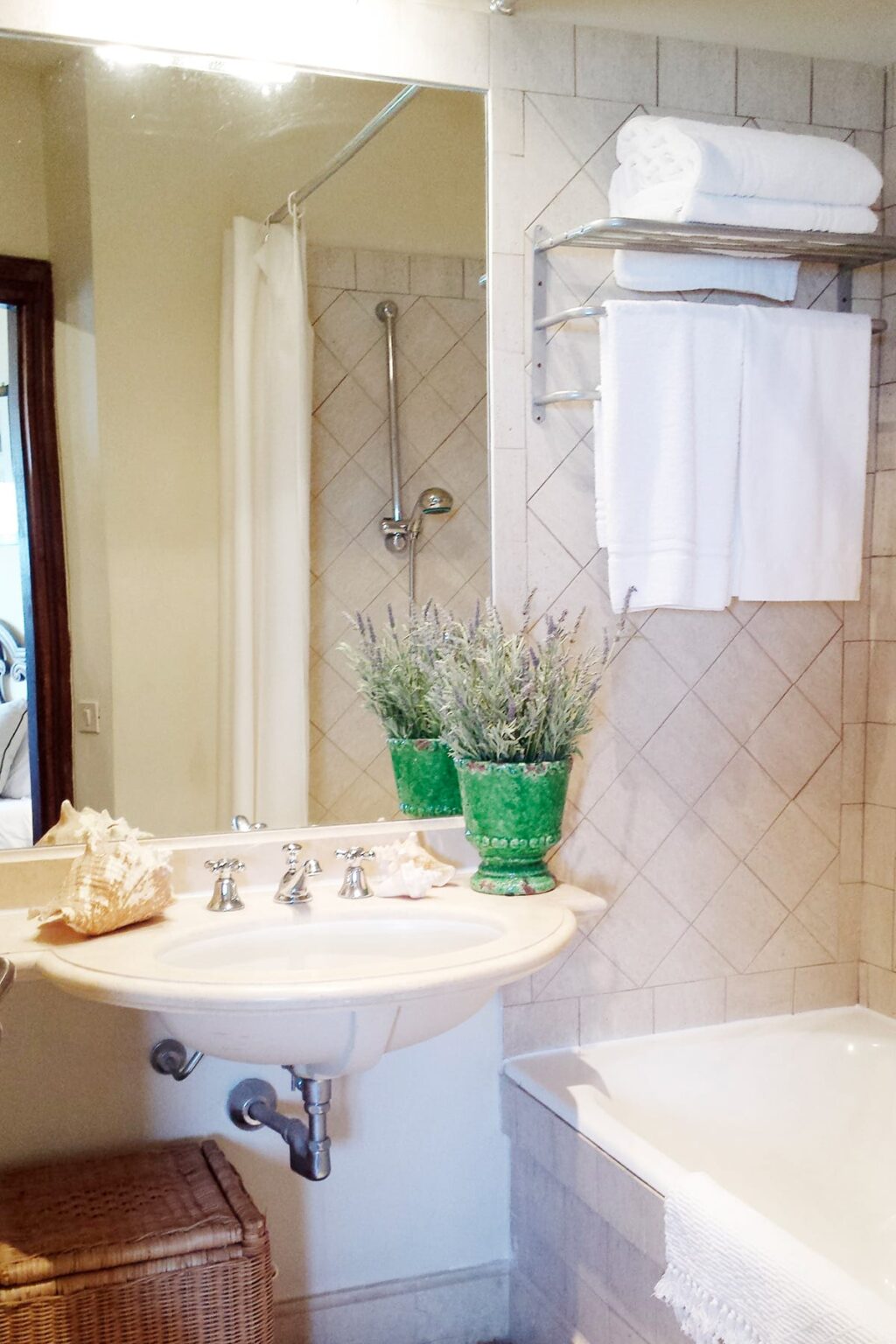 Elegant bathroom interior featuring a marble sink, decorative shell display, and potted lavender plants in green pots, with a shower and white towels in the background. | Only on SopranoVillas