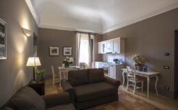 Cozy living space featuring a comfortable sofa, dining area with a table and chairs, and a modern kitchenette, all illuminated by natural light from a window. The walls are painted in a warm neutral tone, enhancing the inviting atmosphere.