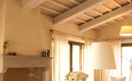 Cozy living room interior featuring wooden beams, soft natural light, a modern lamp, and a fireplace adorned with decorative items, creating a warm and inviting atmosphere.