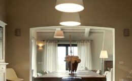 Modern dining room featuring a wooden table, stylish pendant lighting, and large windows with sheer curtains, creating a warm and inviting atmosphere.