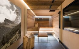 Modern sauna interior featuring wooden paneling, ambient lighting, and a scenic mountain photograph on the wall, designed for relaxation and wellness.