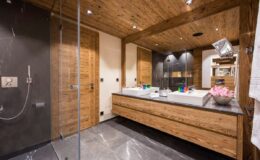 Modern bathroom featuring wooden cabinetry, double sinks, and a spacious shower area with glass enclosure. The design combines natural elements with sleek finishes, creating a warm and inviting atmosphere.