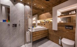 Modern bathroom design featuring a glass shower, wooden accents, a sleek vanity with a sink, and stylish lighting. The space combines natural materials with contemporary elements for a warm and inviting atmosphere.