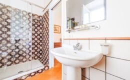 Modern bathroom featuring a glass shower enclosure, patterned wall tiles, a white sink, and a mirror, showcasing a clean and stylish design.