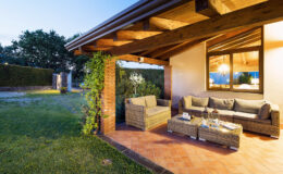Cozy outdoor living space featuring a wicker sofa set under a wooden porch, surrounded by a well-maintained garden at dusk. Perfect for relaxation and entertaining guests.