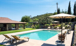 Luxurious outdoor swimming pool surrounded by comfortable lounge chairs and umbrellas, with a scenic view of lush greenery and a charming villa in the background. Ideal for relaxation and leisure activities.