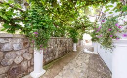 Charming stone pathway lined with lush greenery and hanging flower pots, leading through a serene garden setting.