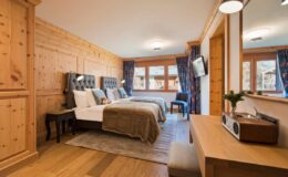 Cozy hotel room featuring two beds, wooden paneling, large windows with scenic views, a stylish desk, and modern amenities, ideal for a comfortable stay.