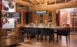 Cozy wooden dining room featuring a large table set for a meal, surrounded by black chairs, with warm lighting and rustic decor elements.