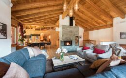 Cozy living room with wooden beams and a stone fireplace, featuring a comfortable sectional sofa, stylish armchairs, and a coffee table adorned with flowers, creating a warm and inviting atmosphere.