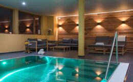 Indoor swimming pool area featuring modern lounge chairs, warm wooden accents, and ambient lighting for a relaxing atmosphere.