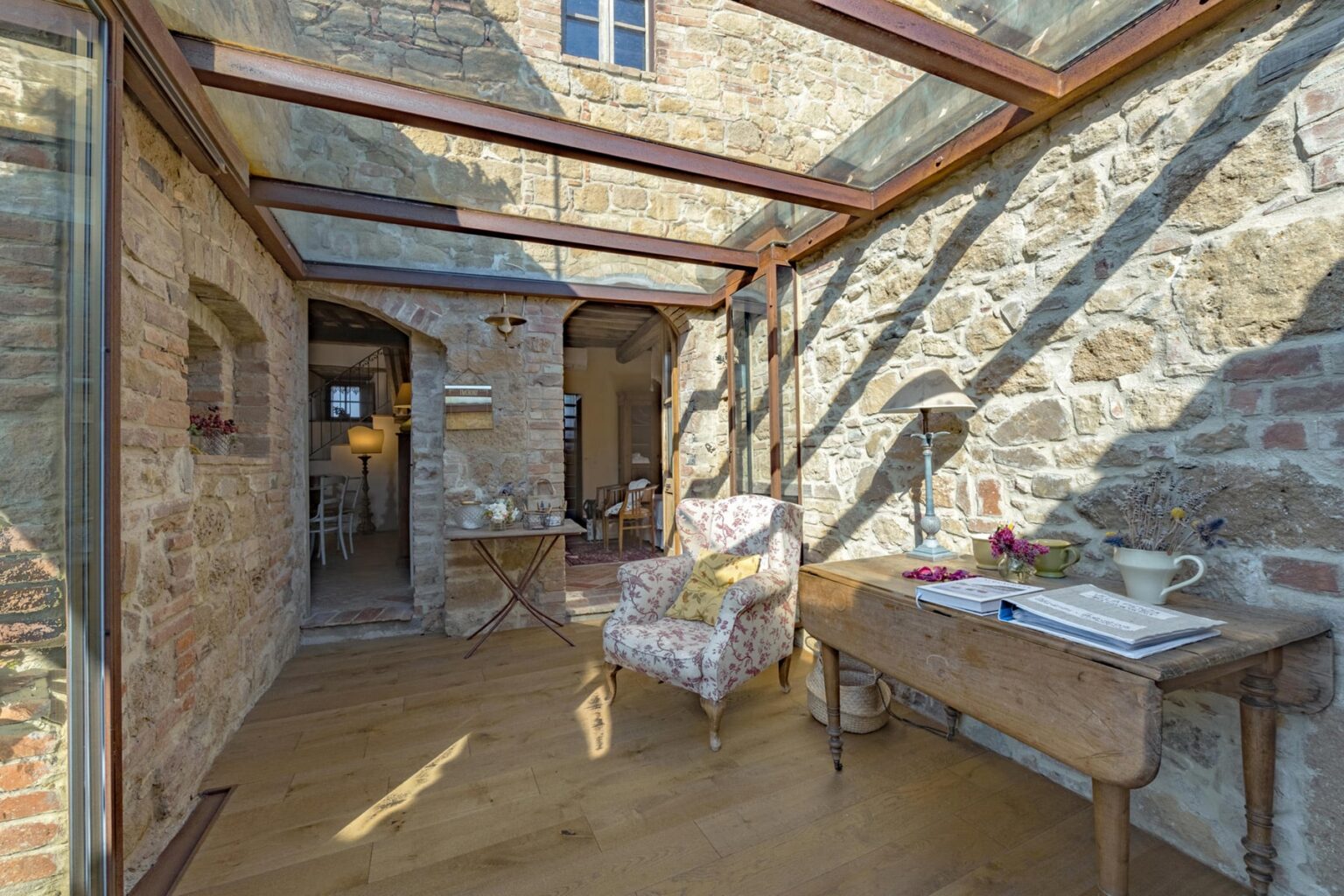 Cozy sunroom featuring a glass ceiling, exposed stone walls, and wooden flooring, furnished with an antique chair and a rustic table. Ideal for relaxation and natural light. | Only on SopranoVillas