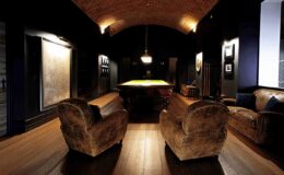 Cozy game room featuring vintage leather armchairs, a billiard table under soft lighting, and dark, elegant decor with artwork on the walls.