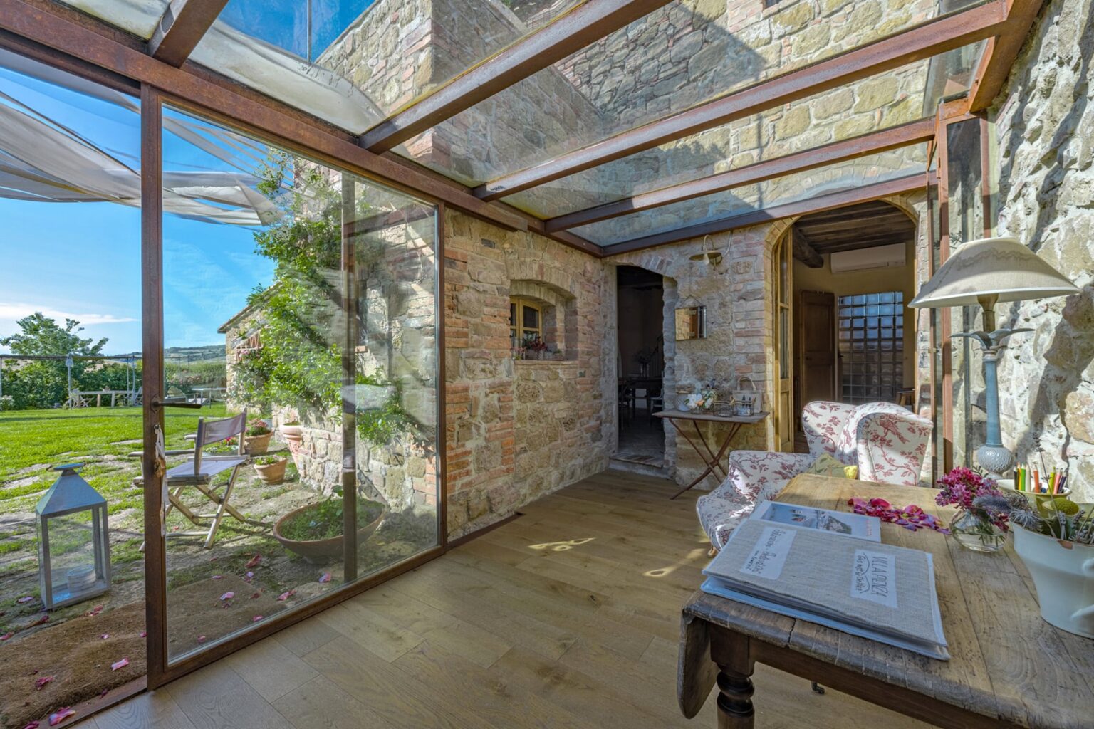 Cozy interior of a modern rustic room featuring stone walls, large glass windows, and wooden flooring, with a view of a lush outdoor garden. Ideal for a serene getaway or home office. | Only on SopranoVillas