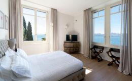 Bright and airy hotel room featuring a king-size bed, large windows with scenic views of the ocean, and stylish decor. The room includes a television and comfortable seating, creating a relaxing atmosphere. Ideal for travelers seeking comfort and tranquility.