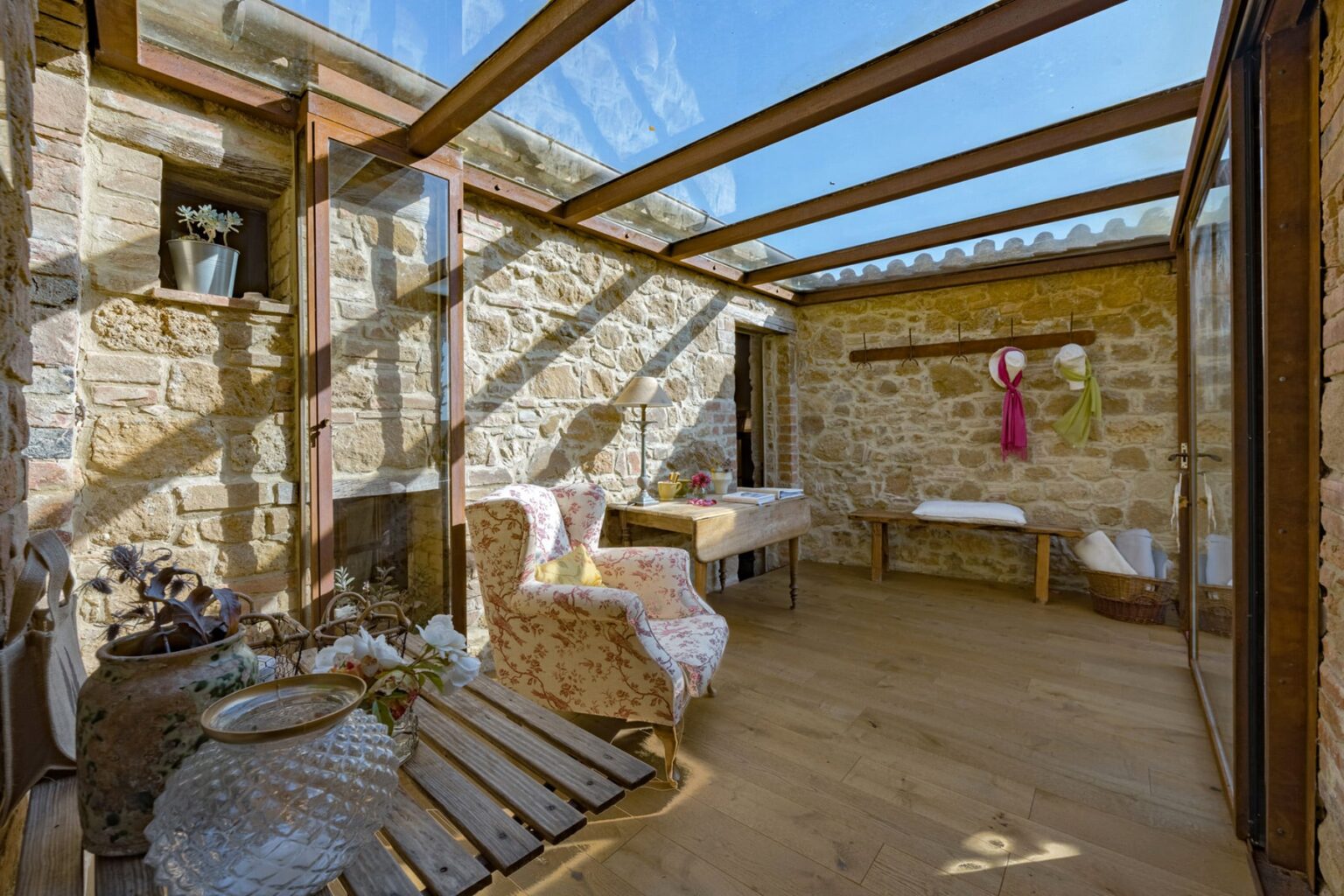 Cozy sunroom featuring stone walls, wooden beams, and large glass panels. Furnished with comfortable chairs and a rustic table, the space is filled with natural light, creating a warm and inviting atmosphere. Ideal for relaxation or enjoying a morning coffee. | Only on SopranoVillas