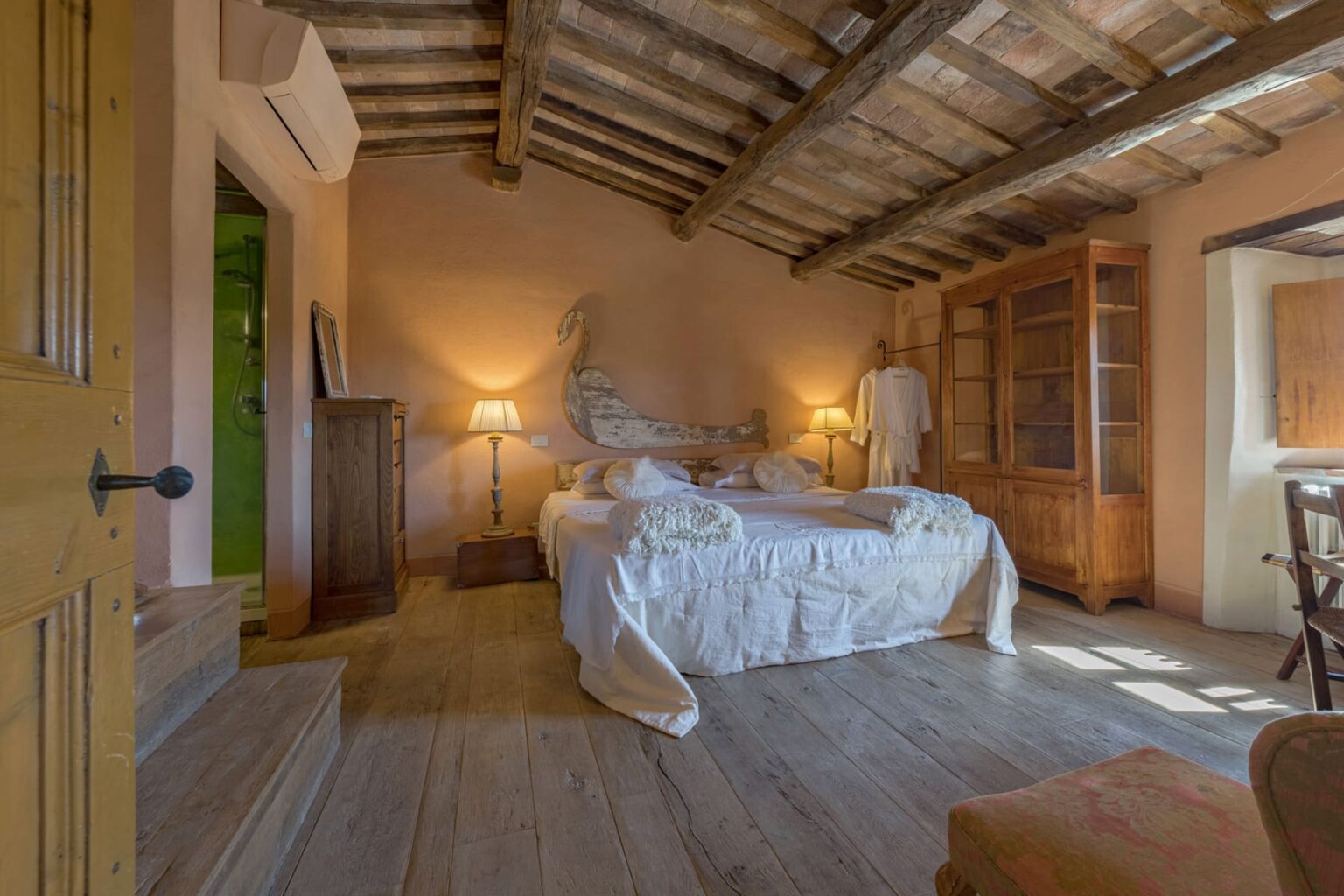 Cozy bedroom with wooden beams, featuring a large bed with white linens, warm lighting from bedside lamps, and rustic wooden furniture, creating a serene and inviting atmosphere. | Only on SopranoVillas
