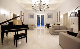 Elegant living room featuring a grand piano, modern furniture, and a stylish chandelier, with large windows allowing natural light to illuminate the space.