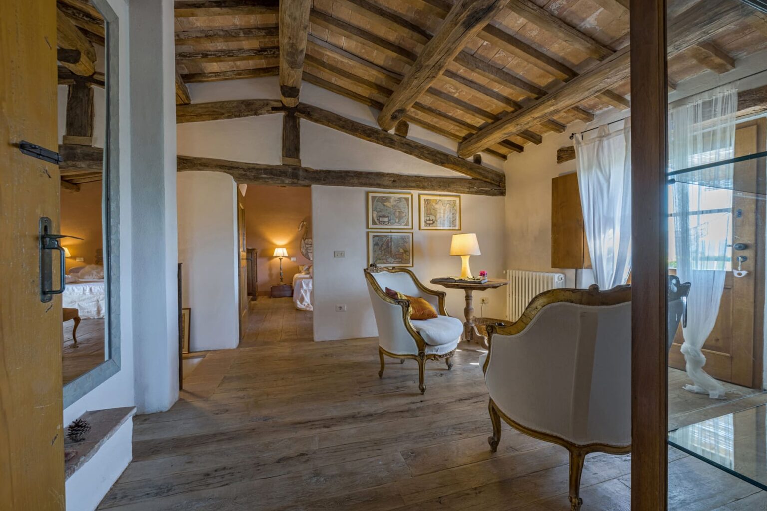 Cozy interior of a rustic room featuring exposed wooden beams, a wooden floor, a small table with a lamp, and elegant seating. The warm lighting creates a welcoming atmosphere, perfect for relaxation. | Only on SopranoVillas