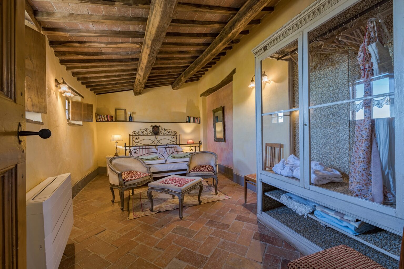 Cozy interior of a rustic bedroom featuring wooden beams, a comfortable bed, stylish seating, and a glass cabinet displaying decorative items. The warm color palette and inviting atmosphere create a relaxing retreat. | Only on SopranoVillas