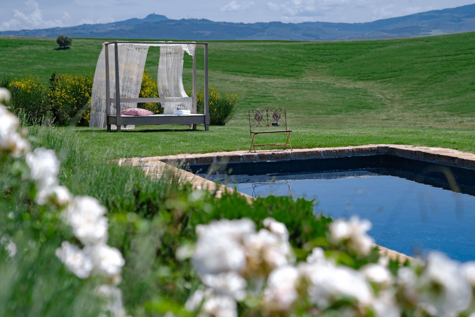 Serene outdoor scene featuring a tranquil swimming pool surrounded by lush greenery and blooming flowers, with a stylish lounge area in the background, perfect for relaxation and leisure in nature. | Only on SopranoVillas