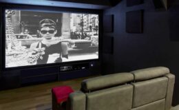 Home theater setup featuring a large screen displaying a classic black and white film scene, with a modern gray sofa in the foreground and dark walls for a cinematic atmosphere.