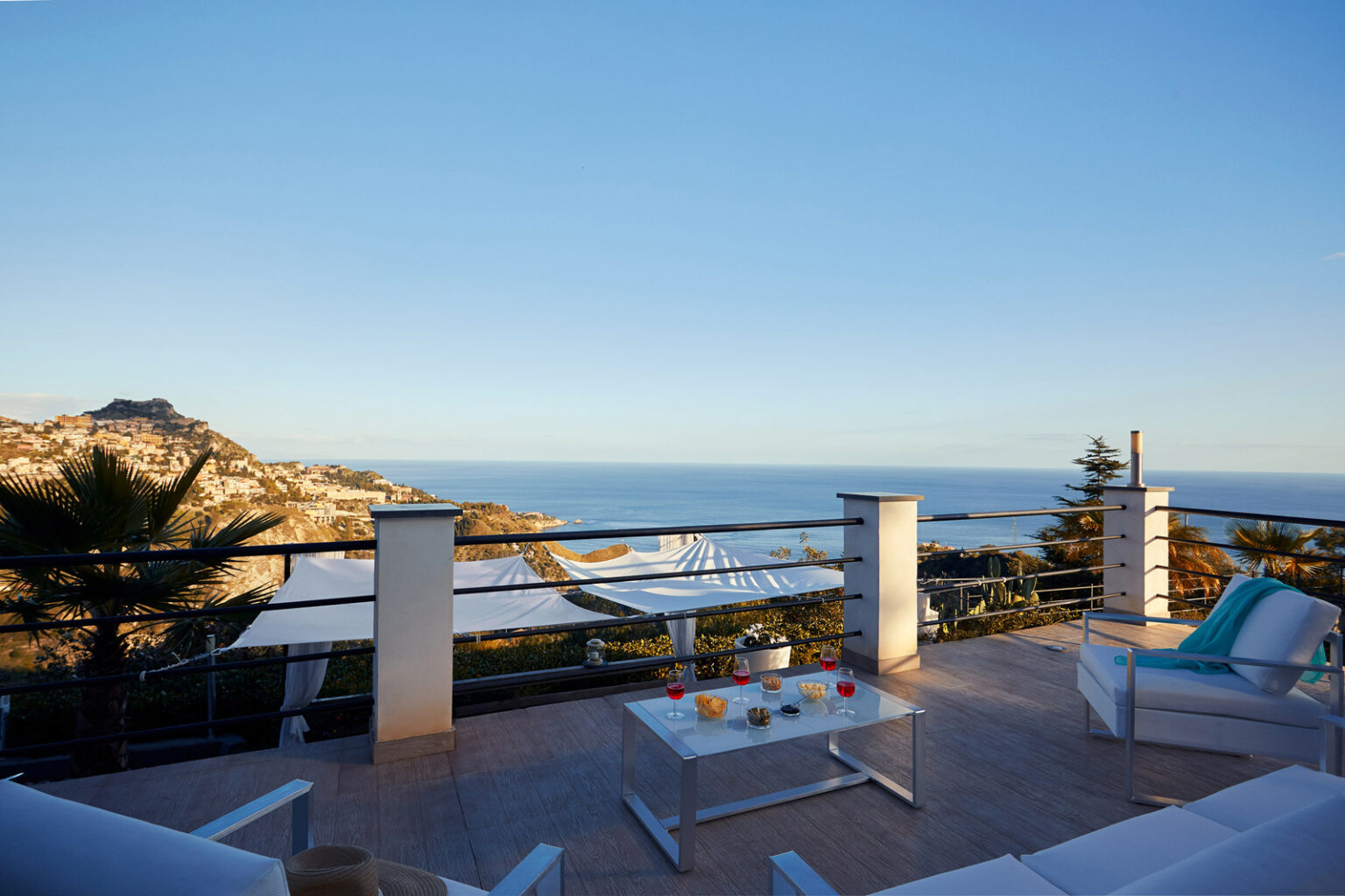 Scenic view from a modern terrace overlooking the ocean, featuring comfortable outdoor seating and vibrant decor, ideal for relaxation and enjoying sunsets. | Only on SopranoVillas