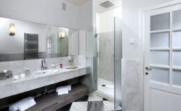 Modern bathroom design featuring a marble vanity, glass shower enclosure, and stylish fixtures. Bright lighting enhances the spacious layout, with neatly arranged towels and a sleek door leading to the room.