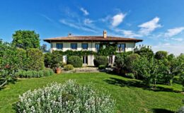Charming two-story house surrounded by lush gardens and trees under a clear blue sky, showcasing a serene outdoor setting ideal for relaxation and nature lovers.