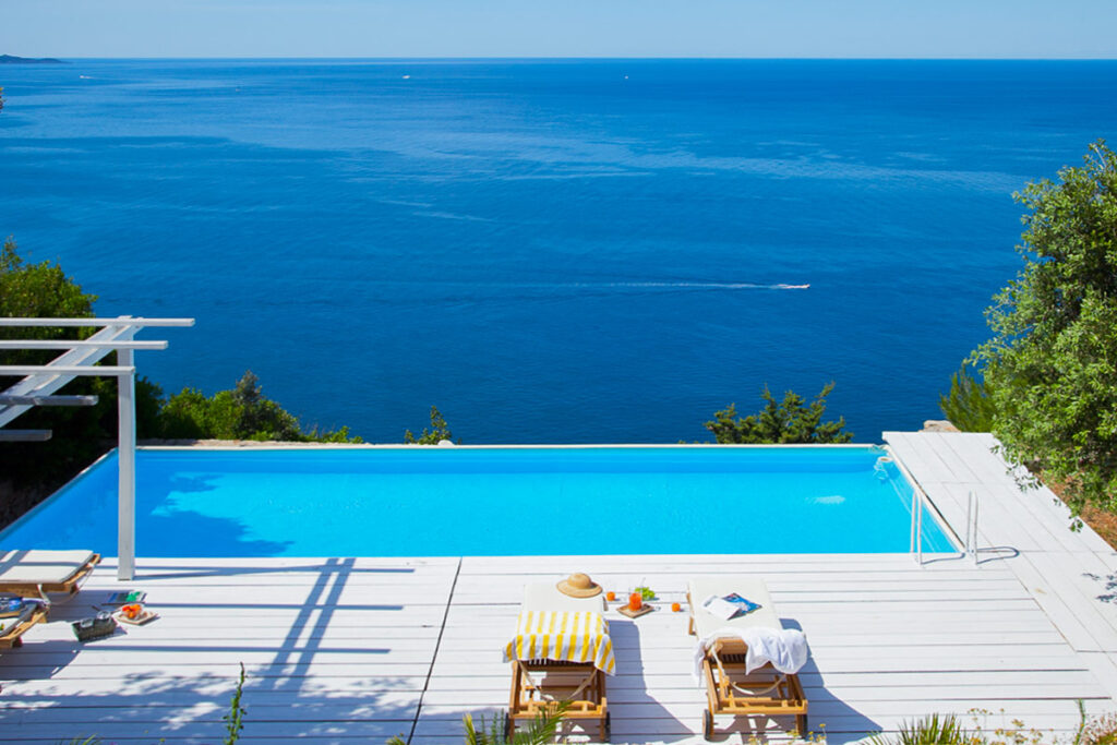 Luxurious infinity pool overlooking the ocean with sun loungers and a clear blue sky, perfect for a relaxing vacation or summer getaway. | Only on SopranoVillas