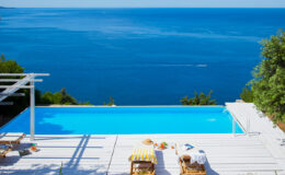 Luxurious infinity pool overlooking the ocean with sun loungers and a clear blue sky, perfect for a relaxing vacation or summer getaway.