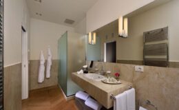 Modern bathroom interior featuring a sleek design with a glass shower, elegant lighting, a stone vanity with a sink, and plush towels.