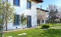 Charming white villa surrounded by lush green grass and blooming trees, showcasing a peaceful outdoor environment with well-maintained landscaping.