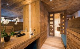 Modern interior design featuring a wooden hallway with natural light, minimalist furniture, and decorative plants. The space includes wooden paneling, recessed lighting, and a stylish workspace, creating a warm and inviting atmosphere.