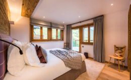 Cozy bedroom featuring a queen-sized bed with decorative pillows, warm wooden accents, large windows for natural light, and a comfortable chair, perfect for relaxation.