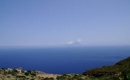 Scenic view of a tranquil blue sea under a clear sky, with a distant volcanic island visible on the horizon, showcasing the natural beauty of the coastal landscape.
